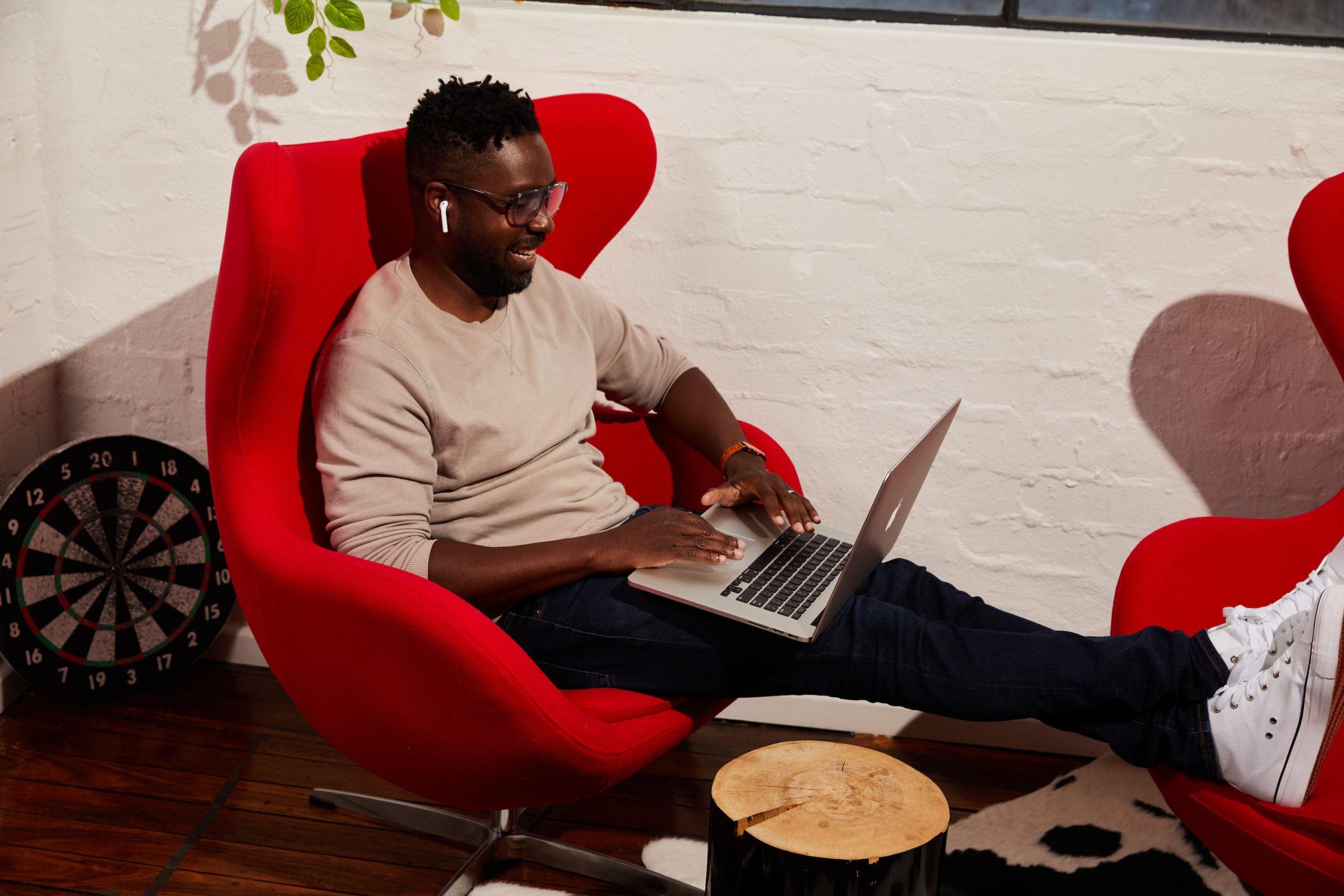 Man sitting in a red chair working on a laptop with a smile.