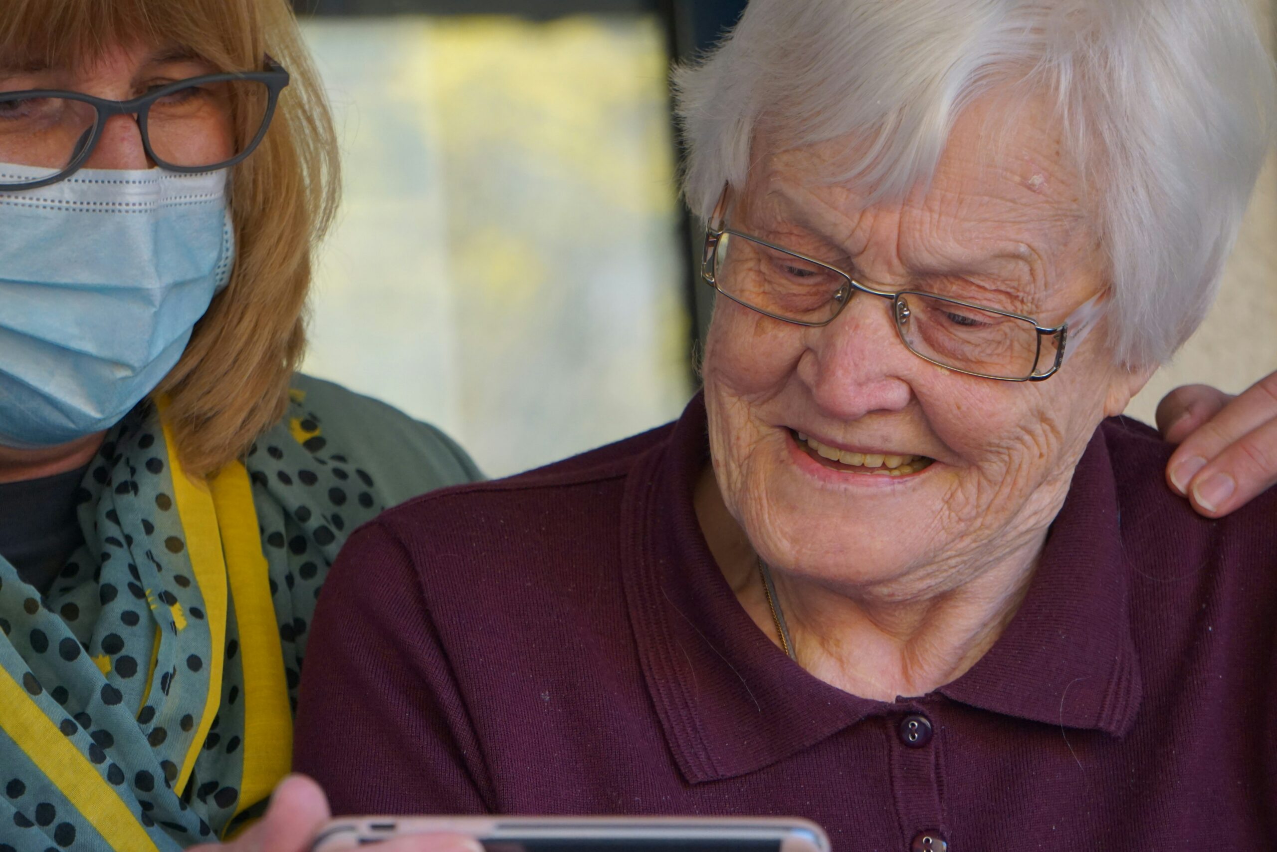 An elderly woman in a maroon collared shirt looking at a phone.