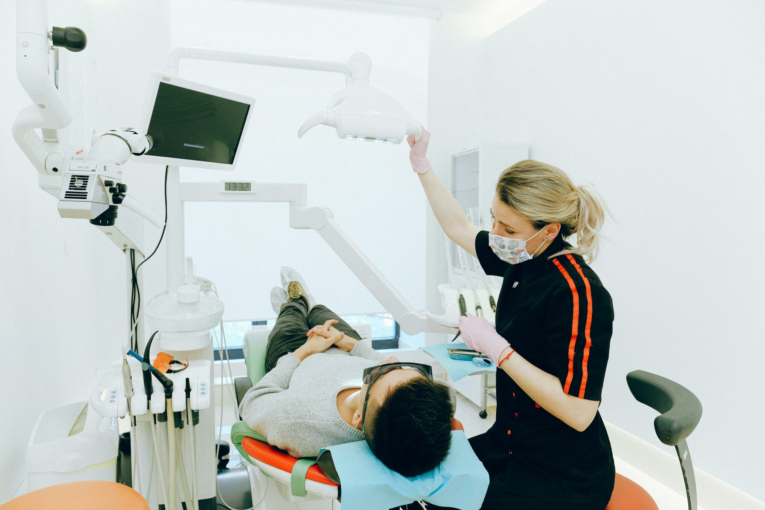 A dentist adjusts an overhead light for a patient lying in a dental chair.
