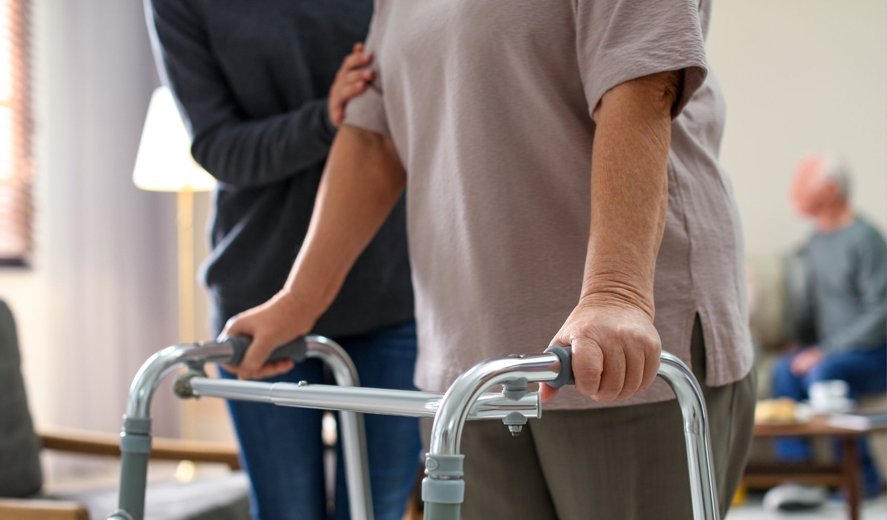 An elderly woman being supported by a caregiver and a walker.