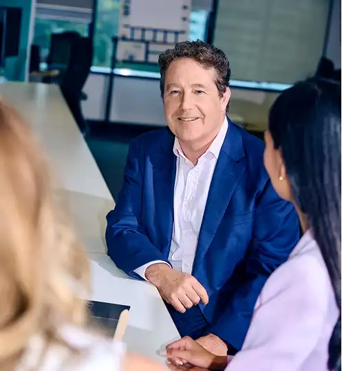 Man in blue suit smiling at two women during a meeting in a modern office. The atmosphere is professional and friendly, with focus on collaboration.