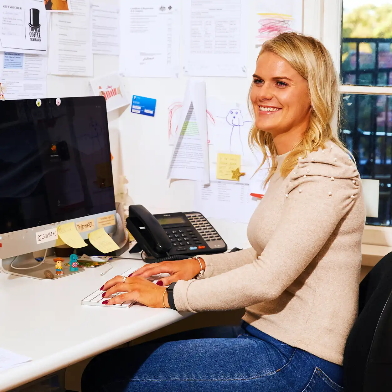 Woman sitting at a desk, focused on her work, with a laptop and notepad in front of her.