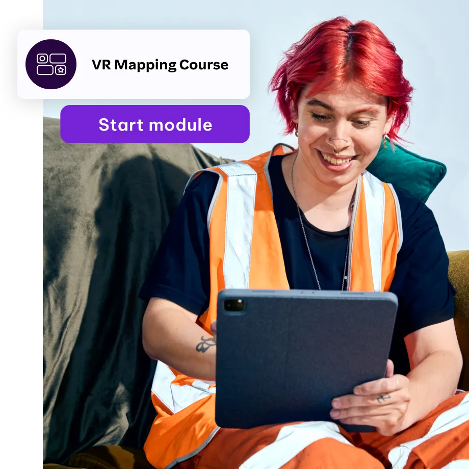 A person with red hair wearing an orange high-visibility vest smiles while using a tablet. A digital overlay shows a "VR Mapping Course" with a purple "Start module" button, suggesting they are engaging in an online training session.