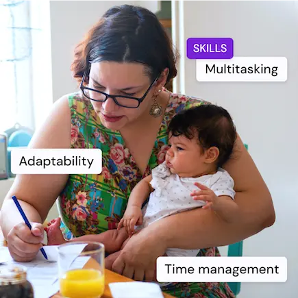 A woman holding a baby while writing on paper, with juice and stationery on the table.