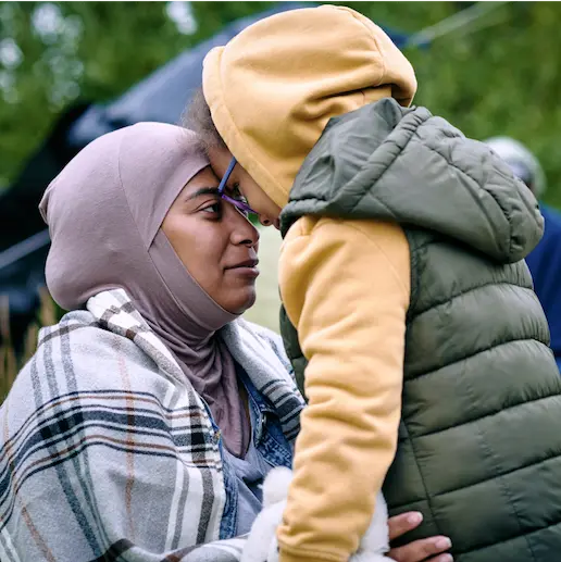 A woman in a hijab and a child in a hoodie touching foreheads affectionately.