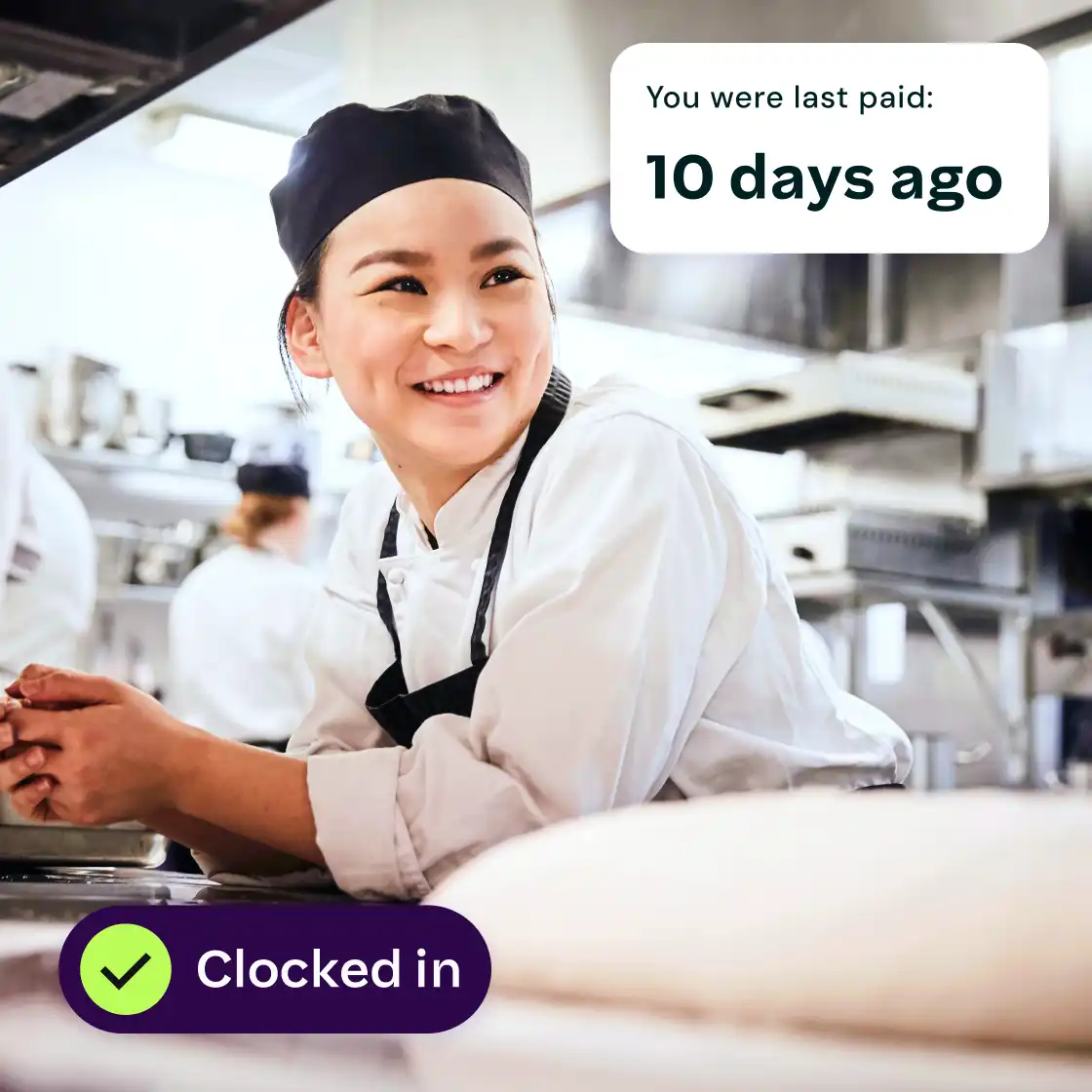 A smiling chef wearing a white uniform and black hat leans on a counter in a professional kitchen. Text overlay: "You were last paid: 10 days ago." A check mark icon and "Clocked in" indicate status.